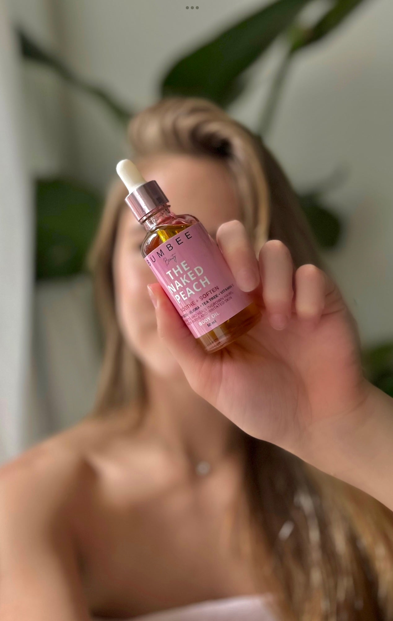 A girl holds a bottle of 'Naked Peach' body oil in front of her face, with the focus on the oil bottle. The image highlights the product as the key solution for addressing skin concerns such as irritation, ingrown hairs, and body acne, promising a clearer complexion and smoother skin
